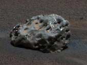 Kovový meteorit s nerovným povrchem usazený v písčitých usazeninách na povrchu Marsu